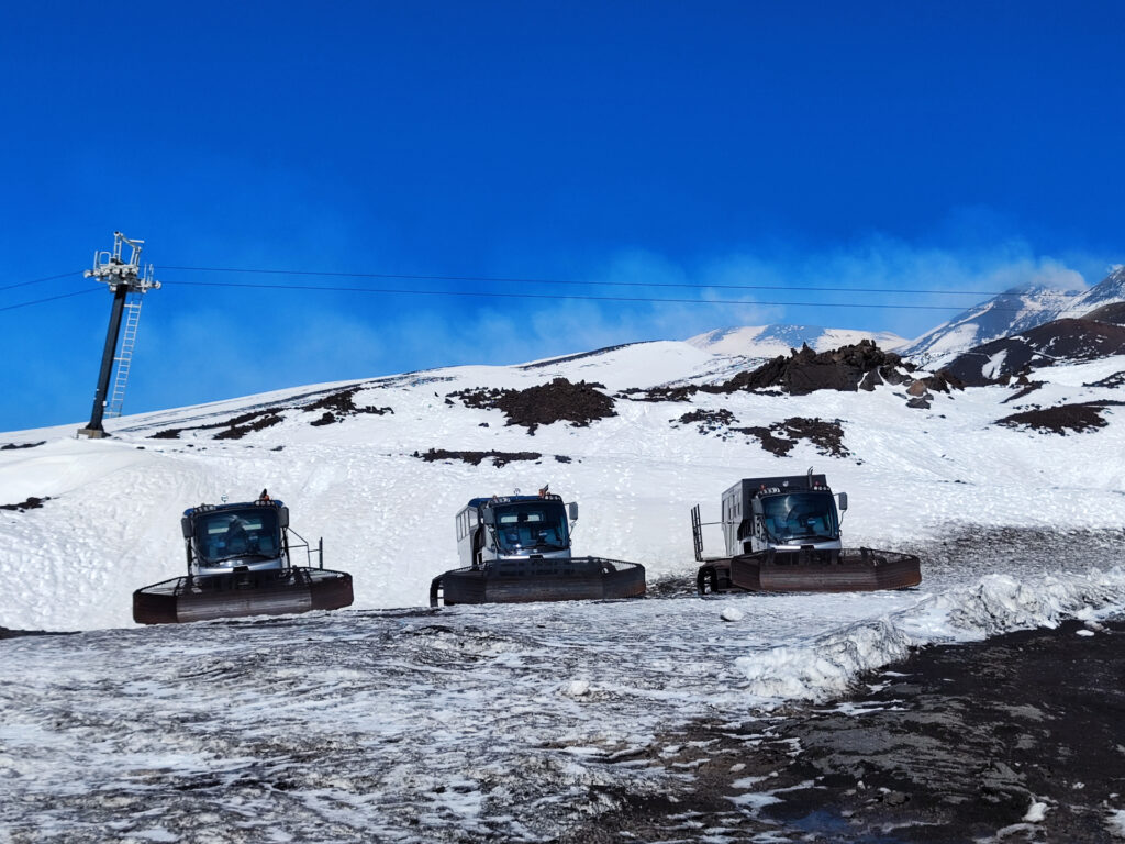 Snowcats parked on the snow-covered landscape of Mount Etna with a cable car tower in the background, embodying the blend of technology and nature.